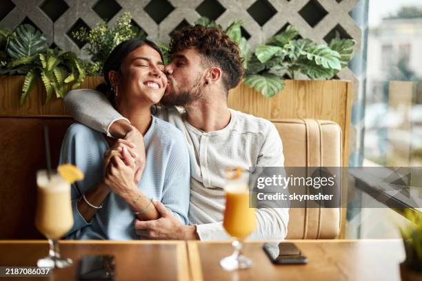 loving man kissing his happy girlfriend in a café. - cheek stock pictures, royalty-free photos & images