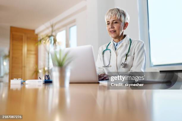 heureux médecin senior travaillant sur ordinateur portable au bureau à domicile. - retraités qui travaillent photos et images de collection