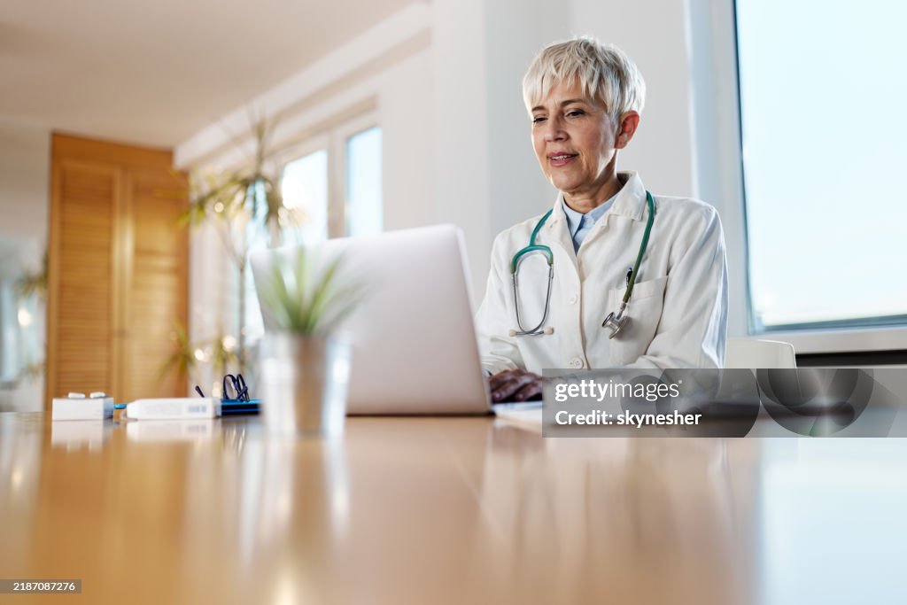 Happy senior doctor working on laptop at home office.
