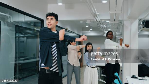 a diverse office team participates in group stretching, promoting workplace wellness, flexibility, and a positive team environment. - wellbeing at work stock pictures, royalty-free photos & images