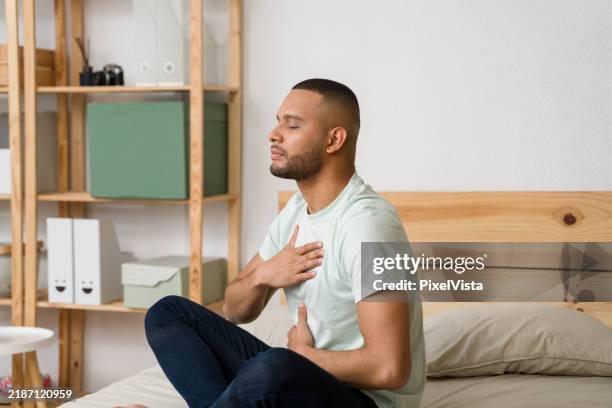 young man practicing deep breathing exercise on bed - exhaling stock pictures, royalty-free photos & images