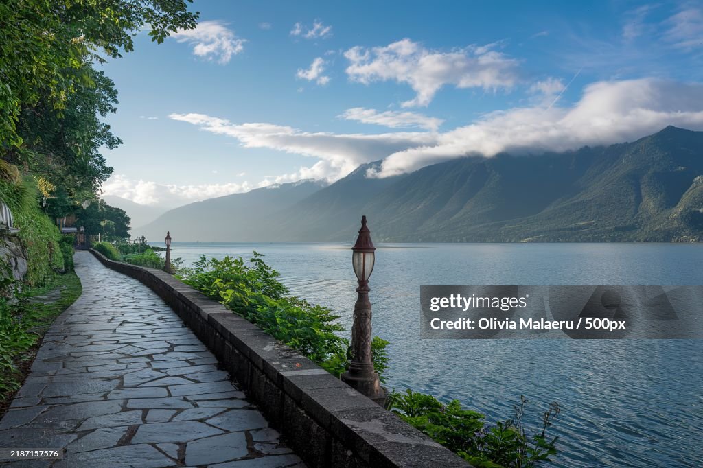 A stone pathway along a lake or ocean shore,With mountains in the background under a blue sky with a few clouds