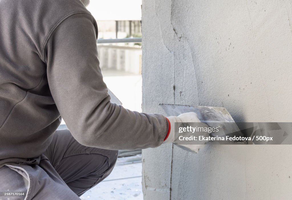 Craftsman uses a float trowel and cement to plaster a house wall Construction process