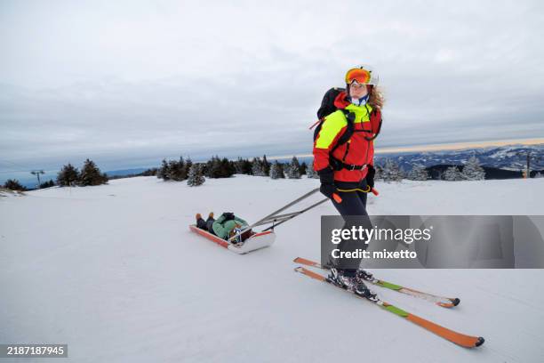 female rescue worker pulling injured snowboarder on sled - ski slope stock pictures, royalty-free photos & images