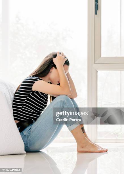 depressed young woman sitting on bedroom floor at home - sitting on ground stock pictures, royalty-free photos & images