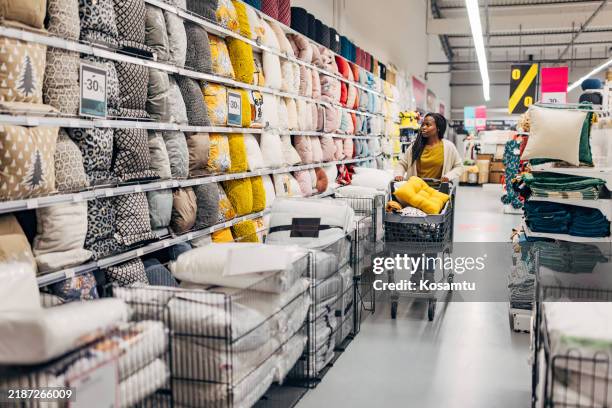 femme noire profitant d’acheter du tissu pour sa nouvelle maison. elle pousse un chariot de supermarché à travers le grand magasin et y met les oreillers, couvertures et autres tissus qu’elle veut acheter - équipement domestique photos et images de collection