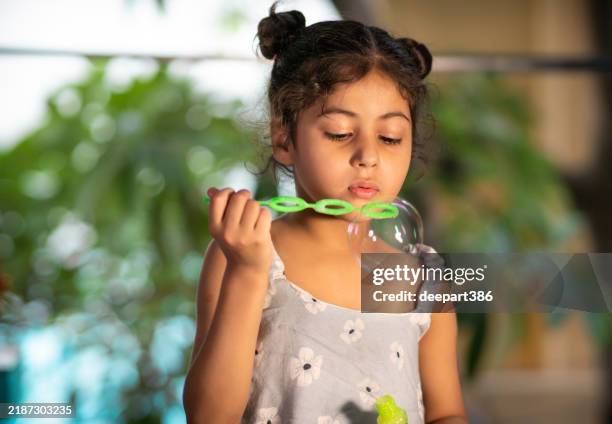 happy little girl blowing bubbles at home - coque atado no topo da cabeça imagens e fotografias de stock