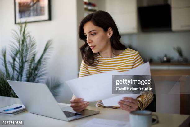 jeune femme qui fait le point sur ses finances à la maison - formulaire des impôts photos et images de collection