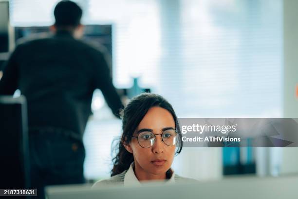 a woman programmer wearing glasses, focused on her tasks in a modern and professional office setting, highlighting determination and innovation. - application programming interface stockfoto's en -beelden