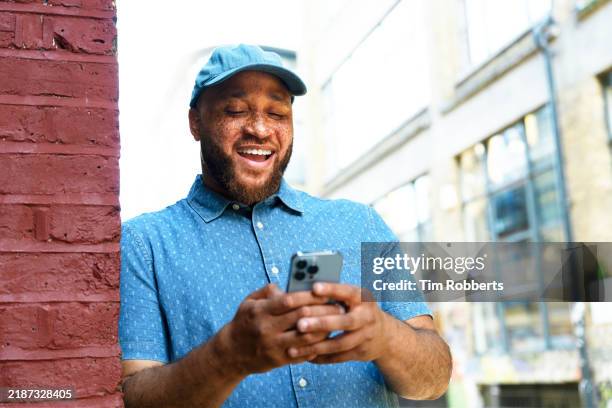 man using smart phone leaning on wall and smiling - men stock pictures, royalty-free photos & images