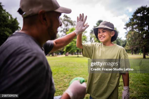 hijo chocando los cinco con su padre durante la recolección de basura en el parque público - responsabilidad social fotografías e imágenes de stock