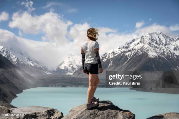 tourist sitting on the shore of tasman glacier terminal lake looking at snow-capped mountains. tasman glacier and lake in mt. cook, south island , new zealand - south island new zealand stock pictures, royalty-free photos & images