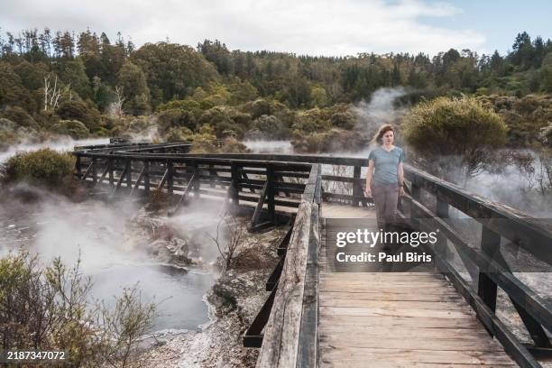 a female tourist walking on the boardwalk across a beautiful volcanic hot spring in rotorua, new zealand - rotorua stock pictures, royalty-free photos & images