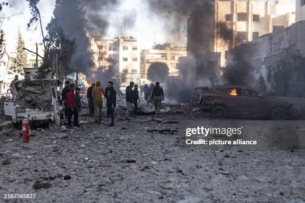 December 2024, Syria, Idlib: Vehicles burn while people inspect the damage caused by a Russian air strike on Idlib University. At least 11 people,...