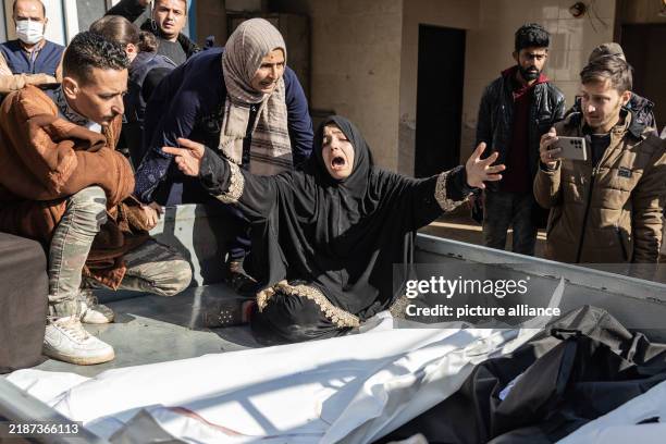 December 2024, Syria, Idlib: A woman mourns in front of the bodies of her relatives, killed in a Syrian regime airstrike on a camp for displaced...