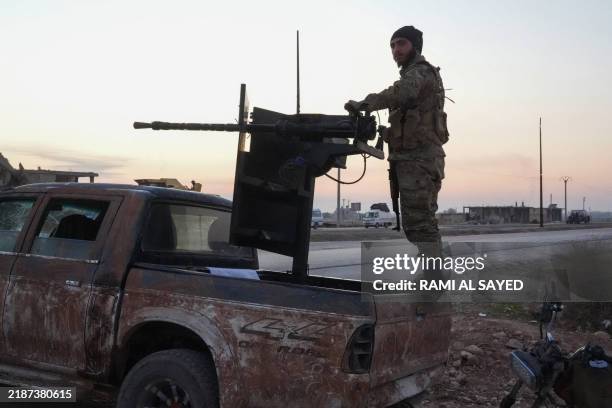 An anti-regime fighter mans a gun on a pick up as displaced Syrian Kurds drive vehicles loaded with belongings on the Aleppo-Raqqa highway to flee...