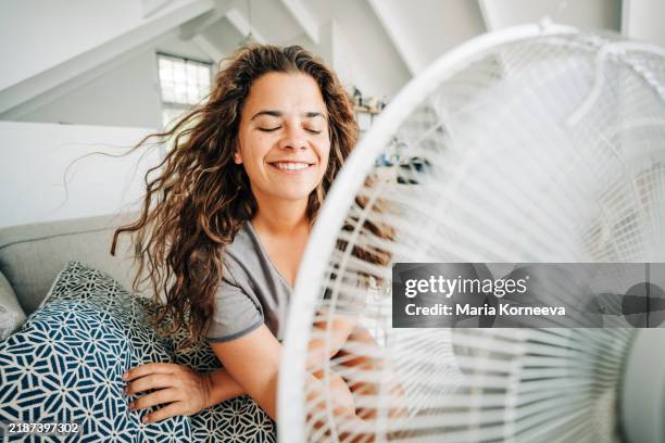 happy contented woman using electric fan at home enjoying fresh air on hot summer day. - ventilateur électrique photos et images de collection