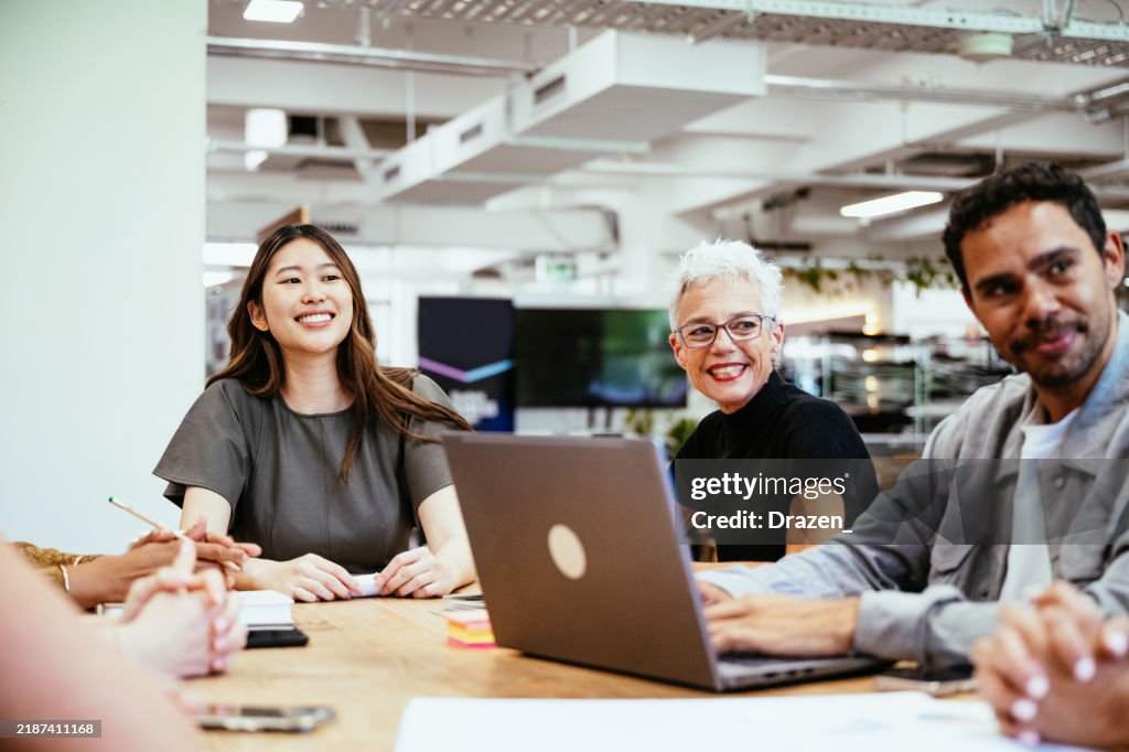 A diverse group of colleagues and business people collaborates on a project at a modern office table surrounded by plants and natural light