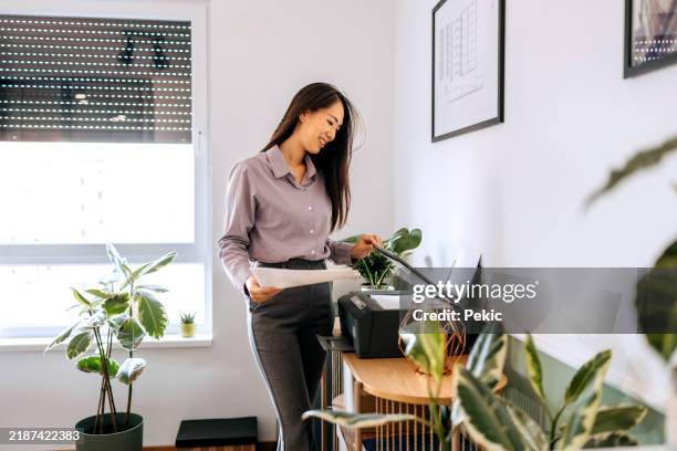 smiling businesswoman using printer at the office - computer printer stock pictures, royalty-free photos & images