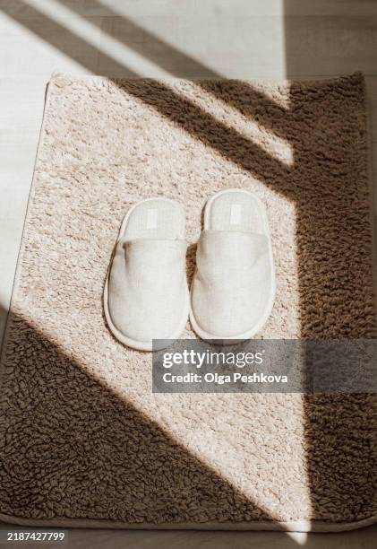 a pair of beige slippers placed neatly on a soft textured bath mat in bright natural light. - slipper stock pictures, royalty-free photos & images