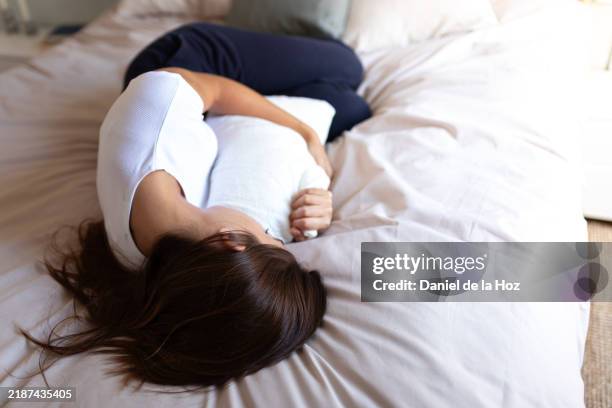 young woman suffering from abdominal pain lying in bed - léiomyome photos et images de collection