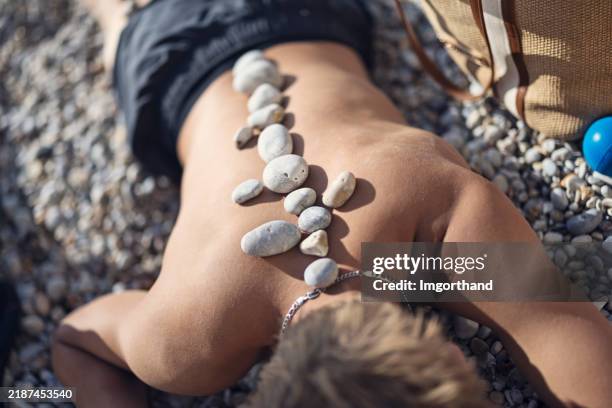 Bot Sunbaking Teenage Boy Sunbathing On A Pebble Beach With Stones Arranged On His ...