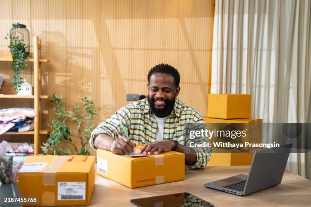 man preparing packages for shipping in home office setting - initiative photos et images de collection
