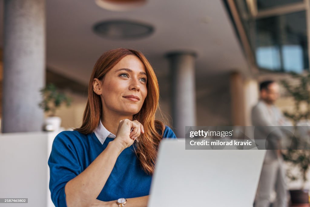 Un retrato de una mujer pensativa sentada en un escritorio de la oficina.