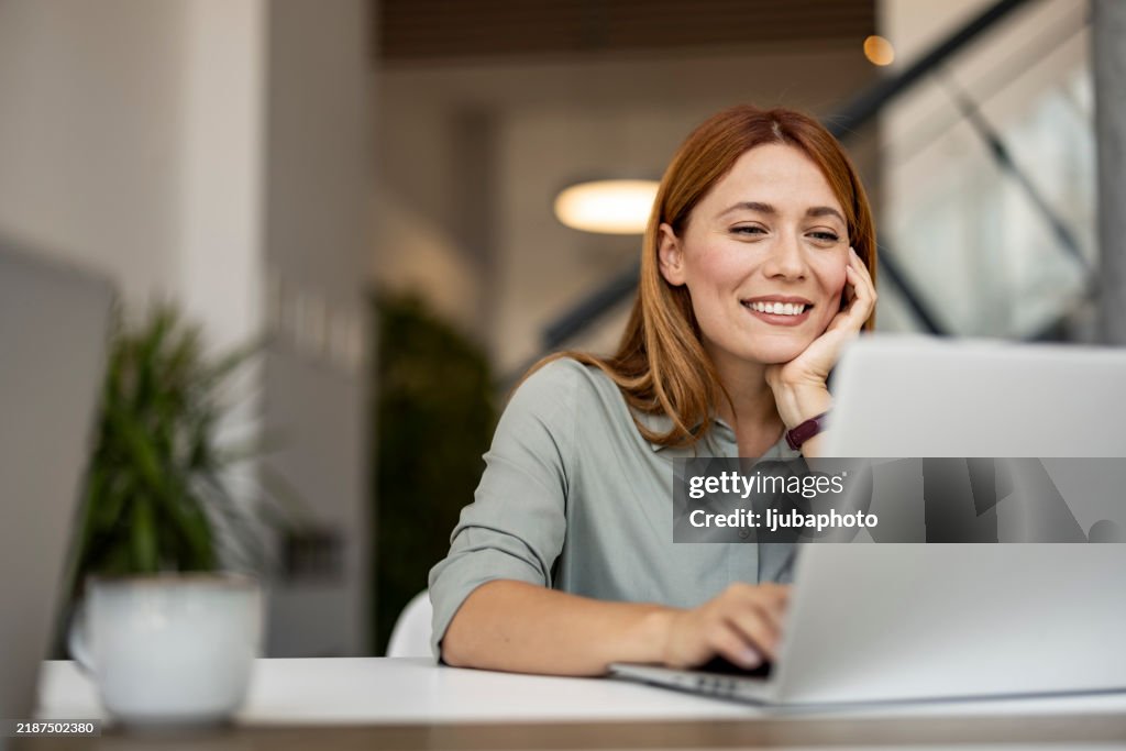 Lächelnde Frau, Die Aus Aus An Laptop In Einem Modernen Arbeitsbereich Arbeitet