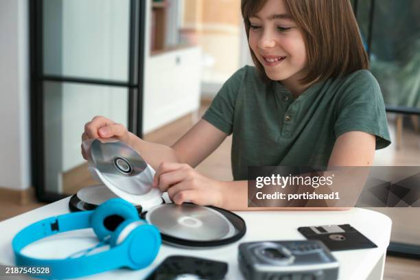 smiling child looking at cd or dvd, vintage cassette tape player, floppy disk and other old school retro portable devices - compact disc stock pictures, royalty-free photos & images