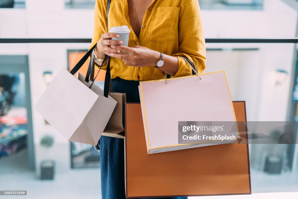 Femme tenant des sacs de courses et du café dans un centre commercial