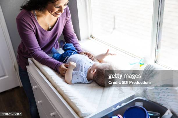 young infant boy looks outside the window while his mom dresses him - changing nappy stock pictures, royalty-free photos & images