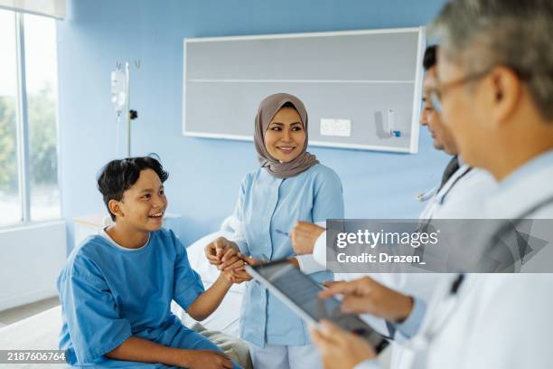 pediatrist doctors examining young teenager boy in the hospital room and making sure his recovery is going well - indonesische etniciteit stockfoto's en -beelden