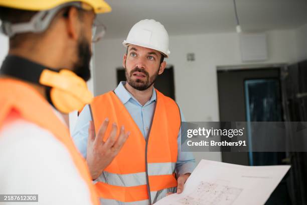 architect and worker reviewing building plans on-site - real estate developer stock pictures, royalty-free photos & images