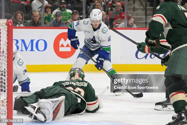 Minnesota Wild goalie Filip Gustavsson freezes the puck as Vancouver Canucks forward Elias Pettersson hunts for a rebound during an NHL game between...