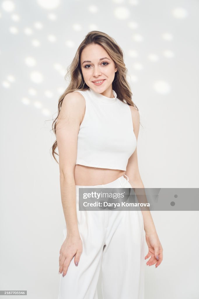 A young woman in white top and pants on white background with lights.