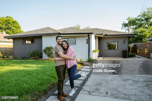 pareja latina madura posando con orgullo frente a una casa recién comprada - ser propietario de vivienda fotografías e imágenes de stock