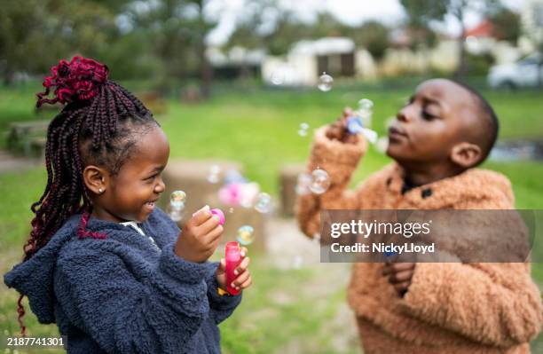 small boy and girl having fun blowing bubbles at park - boy blowing bubbles stock pictures, royalty-free photos & images