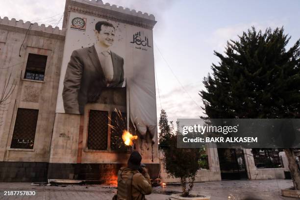 Syrian anti government fighter shoots against a large banner bearing a picture of Syria's President Bashar al-Assad, hanging on the facade of a...