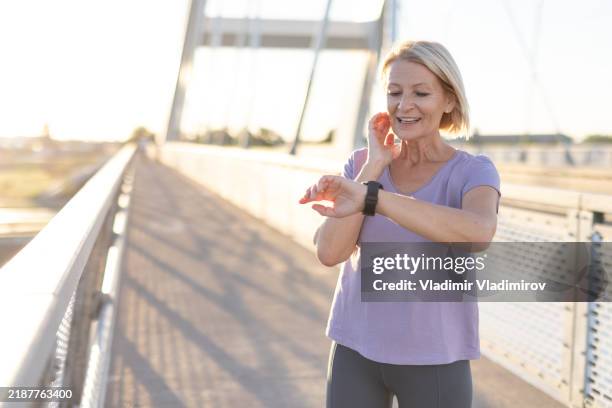 woman checking smartwatch on bridge during workout under sunlight - listening to heartbeat stock pictures, royalty-free photos & images