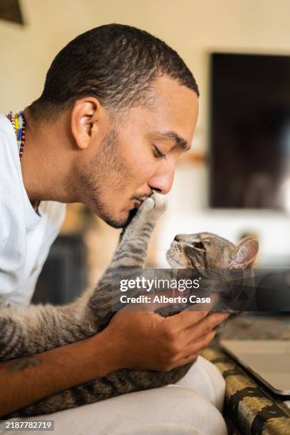 young man kissing his tabby cat at home - man holding cat stock pictures, royalty-free photos & images