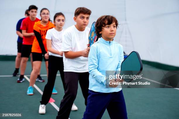 gruppe von kindern, die pickleball mit einem trainer drinnen spielen - mannschaftssport stock-fotos und bilder
