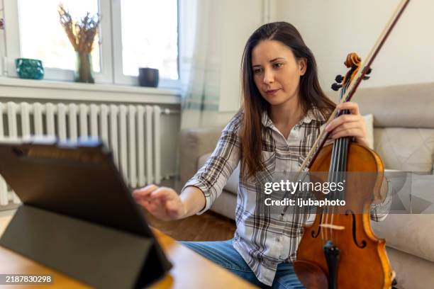 woman learning violin with online resources on a tablet at home - new skill stock pictures, royalty-free photos & images