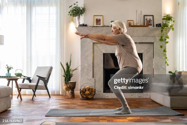 senior woman practicing squats for balance and strength at home - agachar se imagens e fotografias de stock
