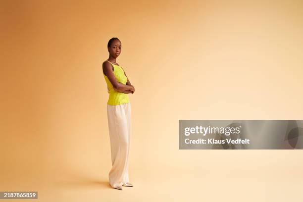 confident young woman standing with arms crossed - fond beige photos et images de collection