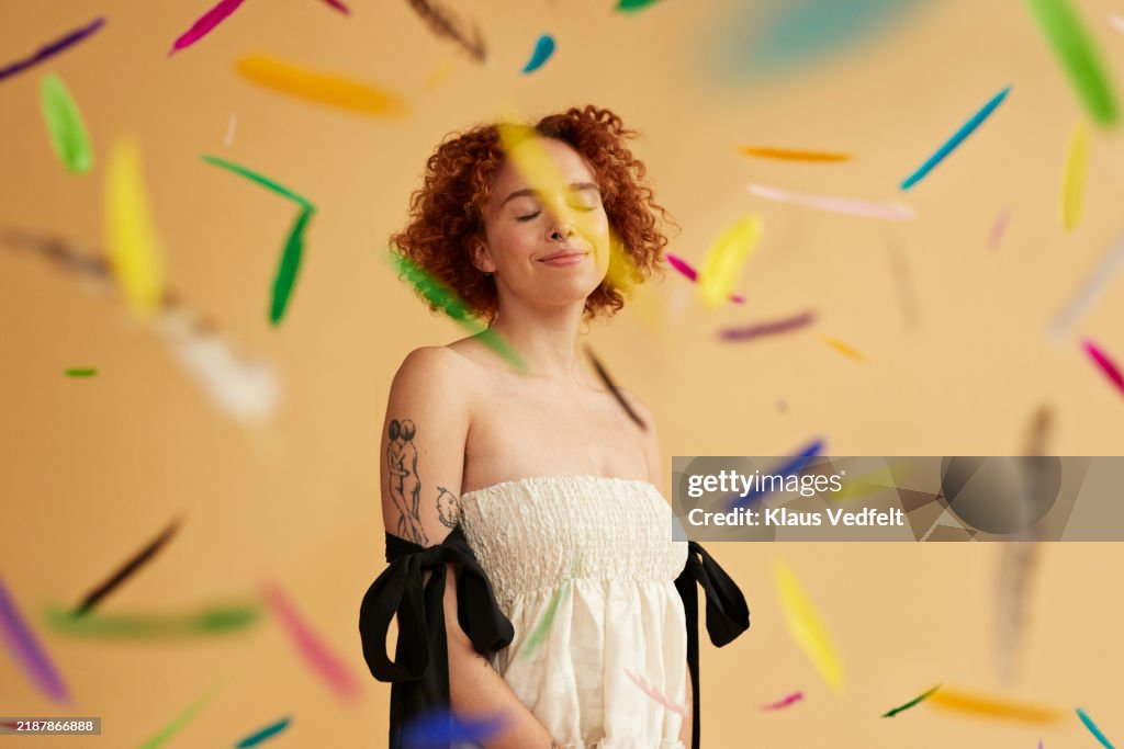 Smiling young redhead non-binary person amidst falling feathers