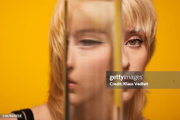 close-up of young blond non-binary person looking through glass - gesicht verstecken stock-fotos und bilder