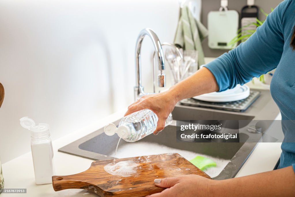 Frau, die Holzschneidebrett mit Essig und Backpulver in der Küchenspüle wäscht
