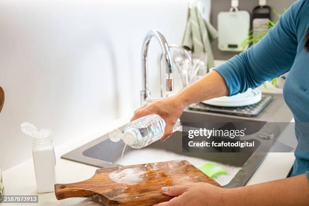 woman washing wooden cutting board with vinegar and baking soda in the kitchen sink - azijn stockfoto's en -beelden