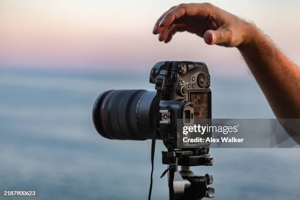 person using modern hi-end digital camera on tripod with ocean background at sunset. - fotografo foto e immagini stock